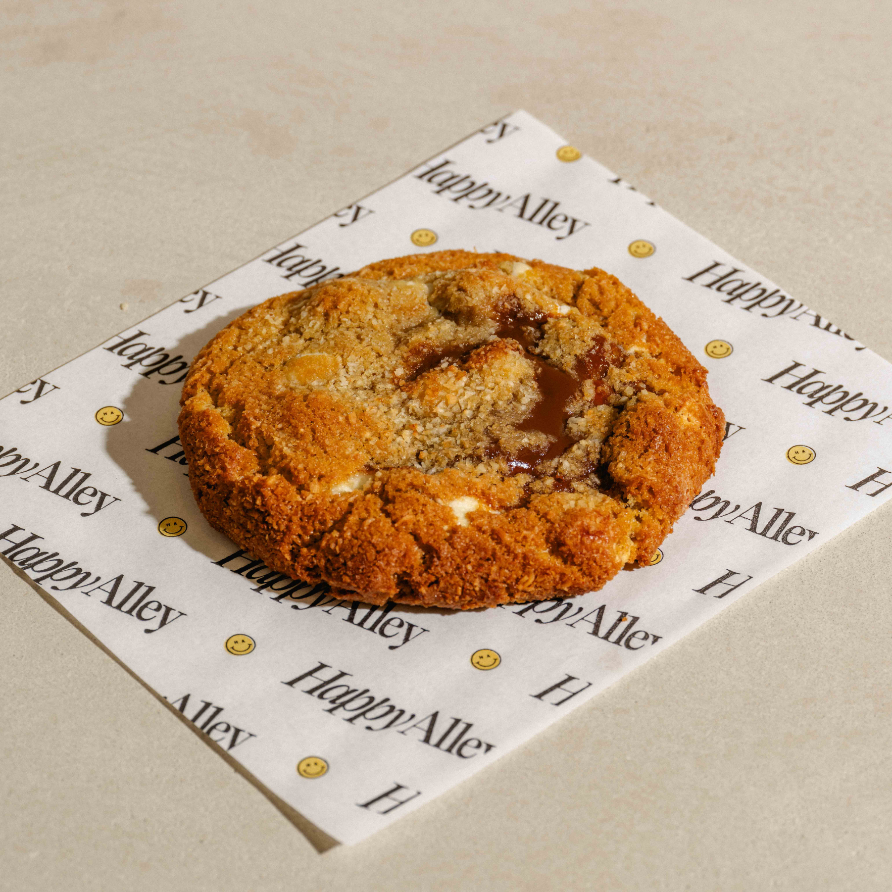 Caramel Dulce De Leche Macadamia Cookie on a piece of paper with Happy Alley branding on a beige background
